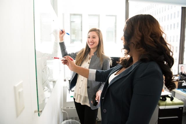 two people discussing their plans in front of a whiteboard