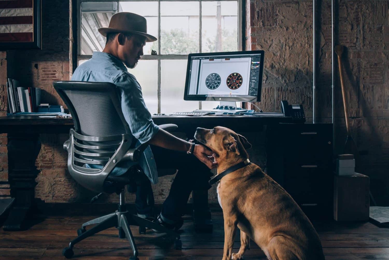 A man seated at a desk with a dog on his lap, representing the integration of pets into a work-from-home lifestyle.