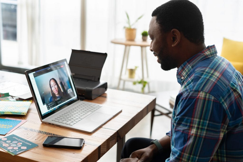 A man working at a desk with a laptop, featuring a woman on the screen, illustrating concepts of employee motivation remotely.
