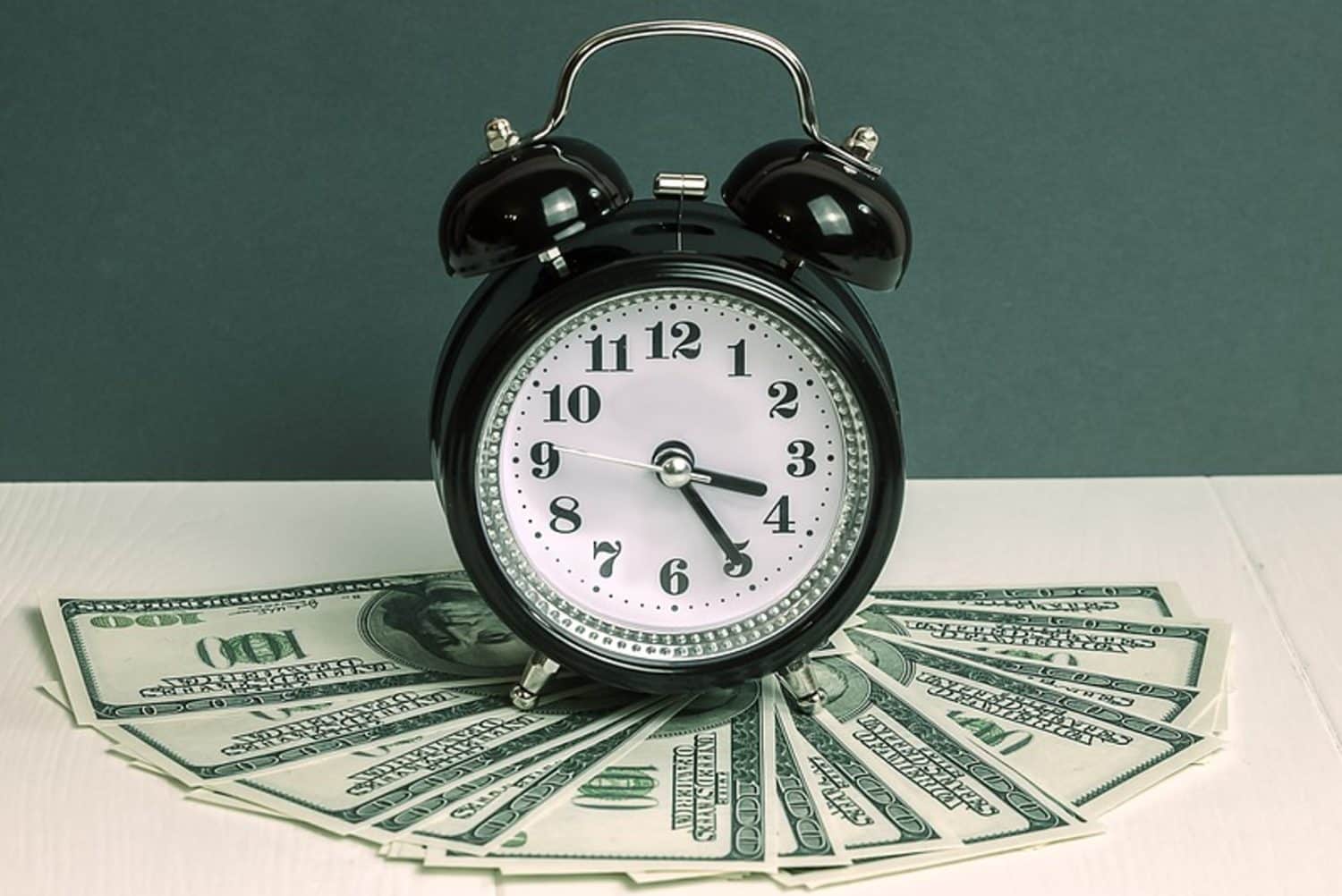A black alarm clock on a money stack, illustrating the importance of time management in reducing business expenses.