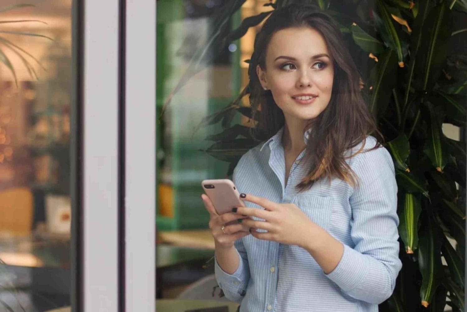 A woman in front of a window checks her phone, engaged in thoughts about event management platforms.
