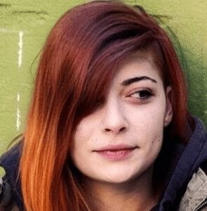 A headshot of a woman with striking red hair and a black jacket, embodying the spirit of Gen Z in coworking spaces.