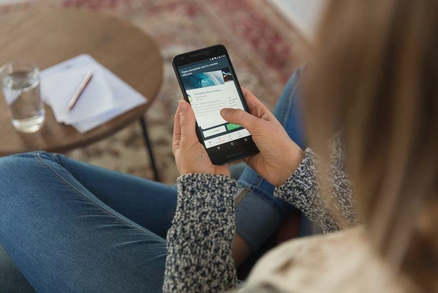 A woman comfortably sitting on a couch, using her phone, highlighting important digital nomad essentials for travelers.