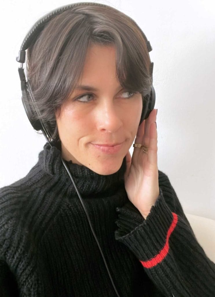 A woman in a cozy sweater wearing headphones, engaged in a podcast production setting.
