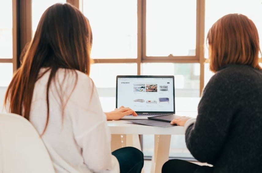 Two women seated at a table with laptops, illustrating the partnership of small businesses and startups in coworking environments.
