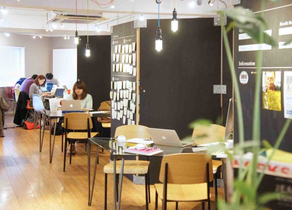 A dynamic scene in a Tokyo coworking space, with individuals seated at desks and tables, promoting teamwork and creativity.