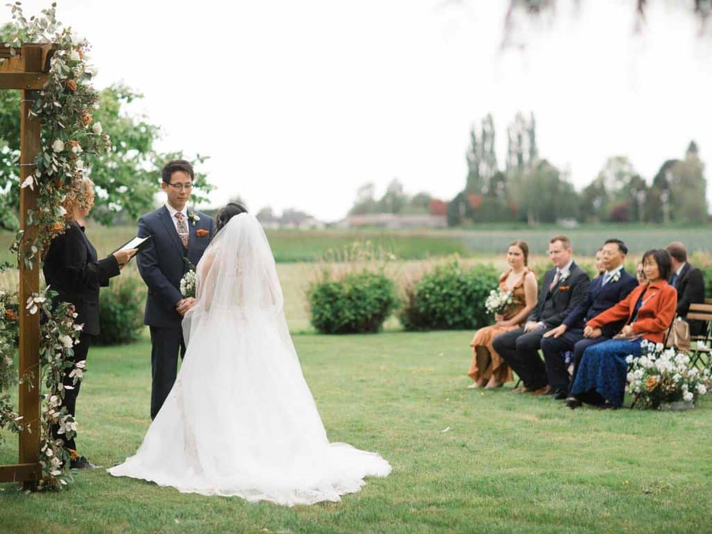 A picturesque wedding ceremony on the grass, with attendees observing the heartfelt moments of the couple's special day.