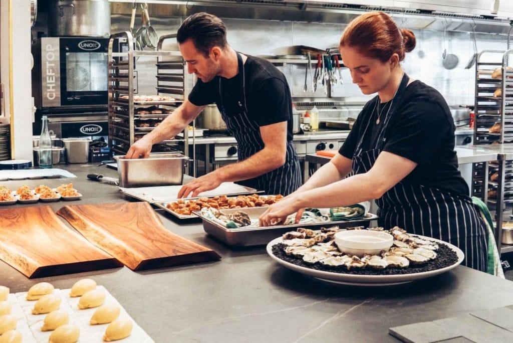 Two chefs skillfully preparing dishes in a bustling commercial kitchen, showcasing teamwork in a catering business environment.