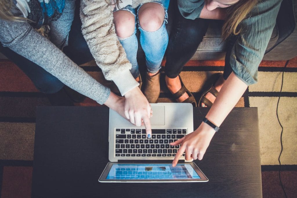 Three women seated on a couch, focused on a laptop, exemplifying teamwork and collaboration in a relaxed environment.