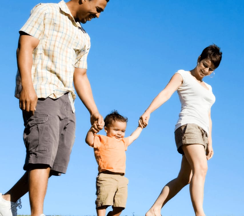 A family strolls through a green field, holding hands and sharing a moment of connection and happiness outdoors.