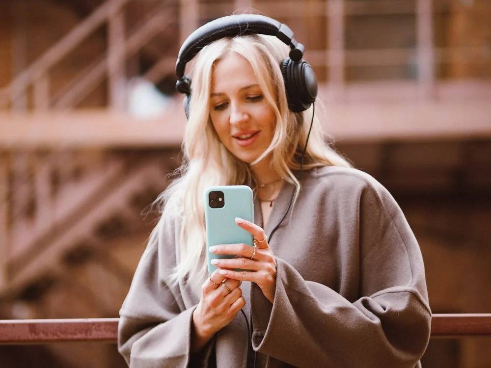 A woman wearing headphones and holding a cell phone, representing the importance of video marketing for small businesses.