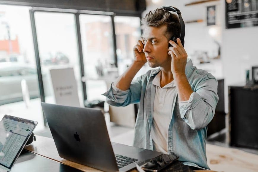 A man at a desk with a laptop and headphones, representing the relationship between music and work efficiency.
