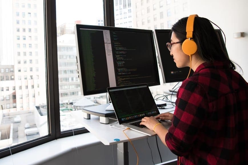 A woman at her desk with two monitors and headphones, exemplifying the relationship between music and work efficiency.