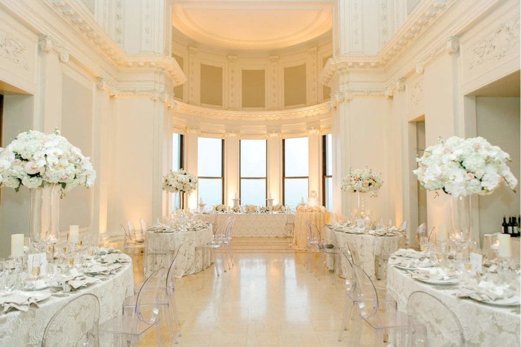 A spacious wedding reception at James Leary Flood Mansion, featuring elegant white tables and chairs in a beautifully decorated room.