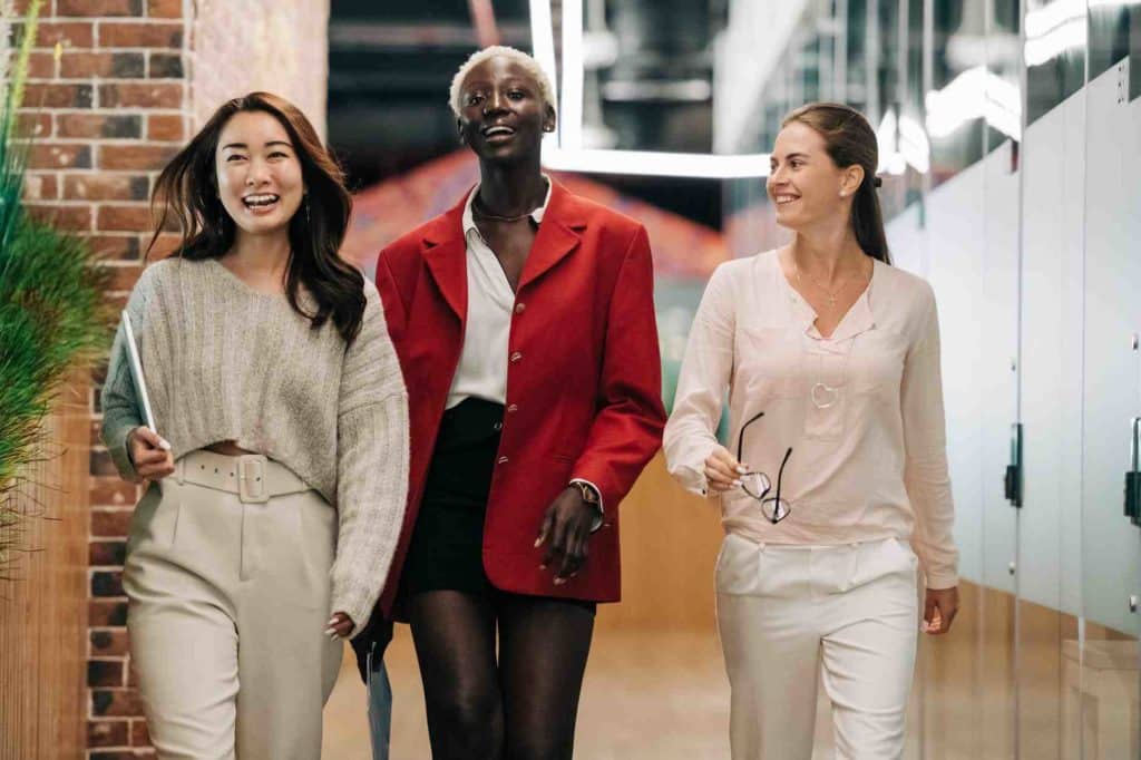 Three women representing different ethnicities walking through an office corridor, highlighting the importance of racial equity.