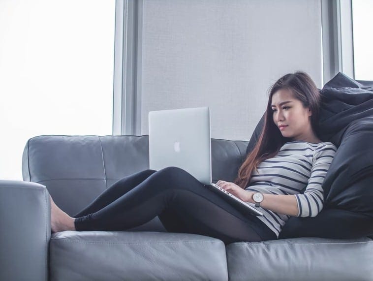 A woman comfortably seated on a couch, using a laptop to work from home, illustrating the remote work trend.