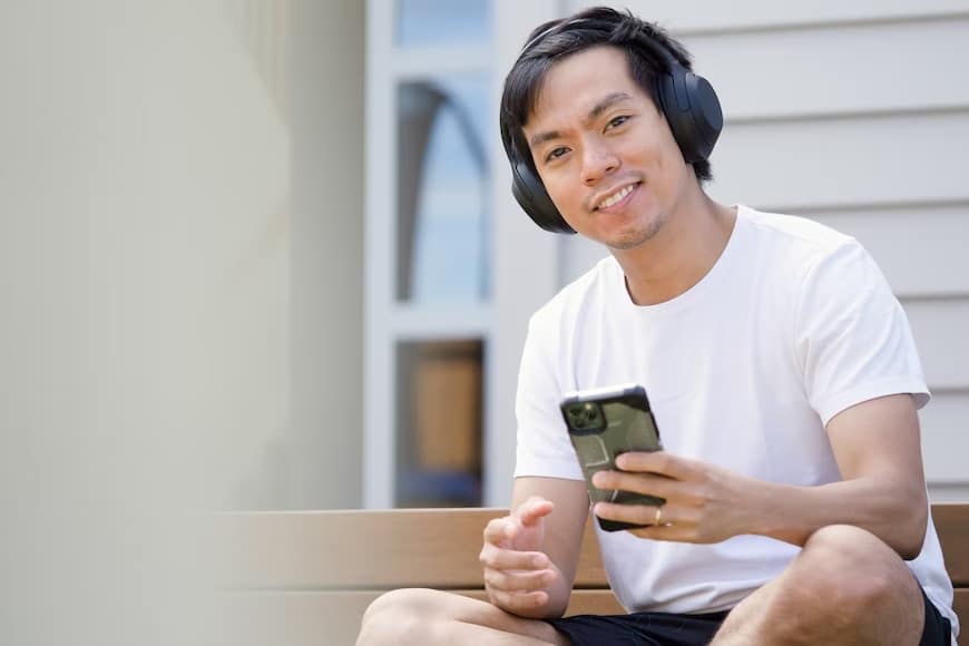  A man wearing headphones on a bench uses his phone, highlighting the growing trend of podcast advertising.
