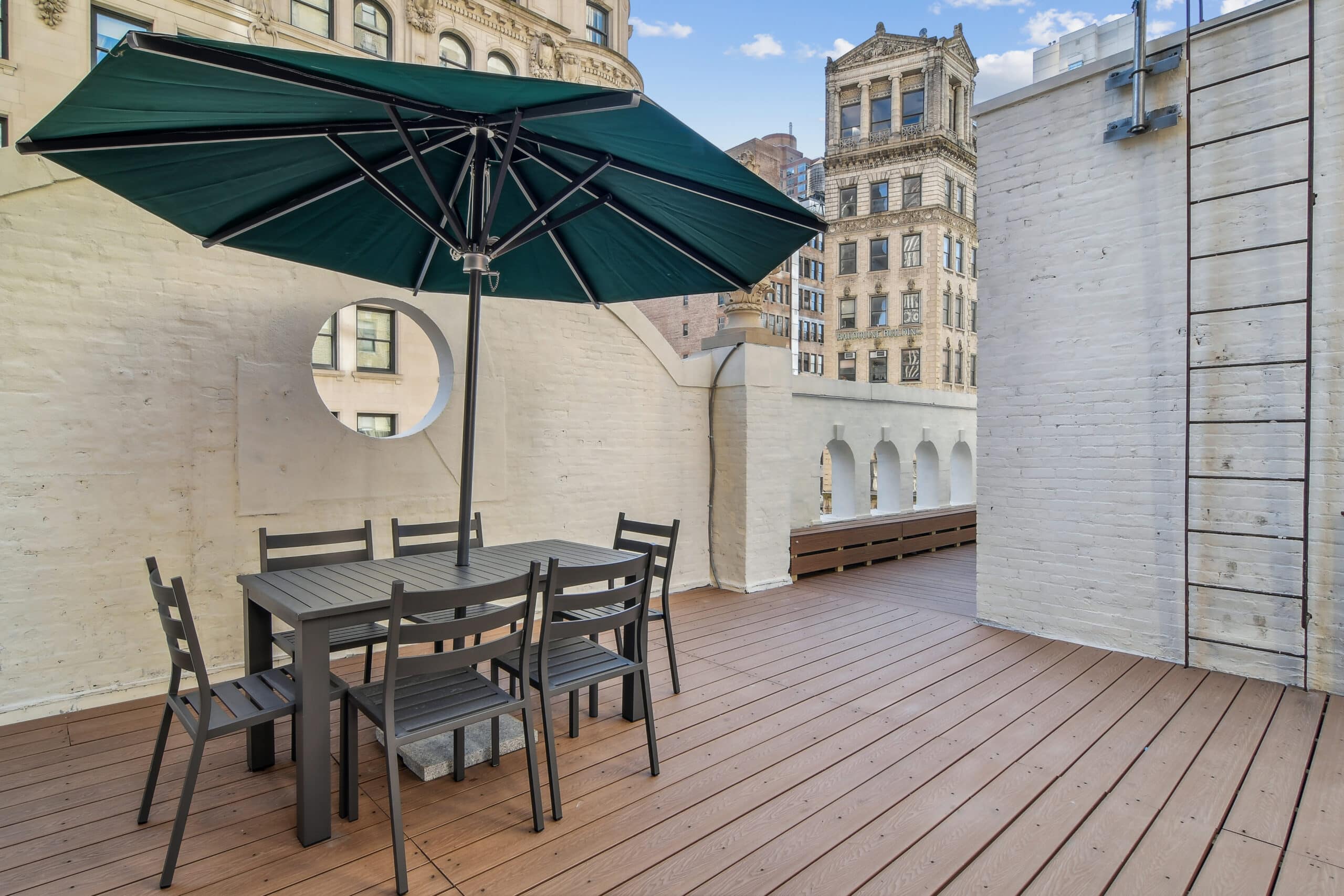 A cozy patio featuring an umbrella and chairs set on a wooden deck, perfect for relaxation at The Farm Soho - Nomad Rooftop.