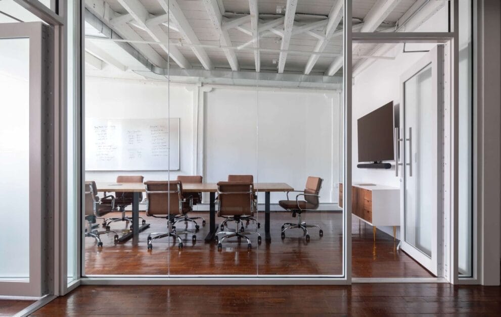 Contemporary office space showcasing a large glass wall and warm wooden flooring, perfect for meetings and presentations.